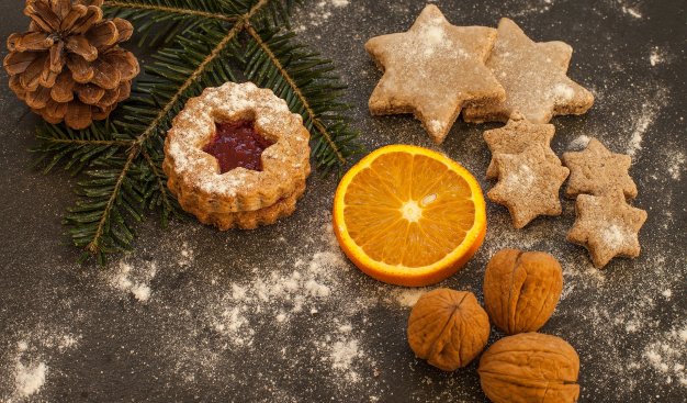Świąteczne ciasteczka w kształcie gwiazdek, plaster pomarańczy i orzechy  oraz gałązka choinki.