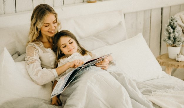 Kobieta razem z dziewczynką leżą na łóżku z otwartą książką przed oczami