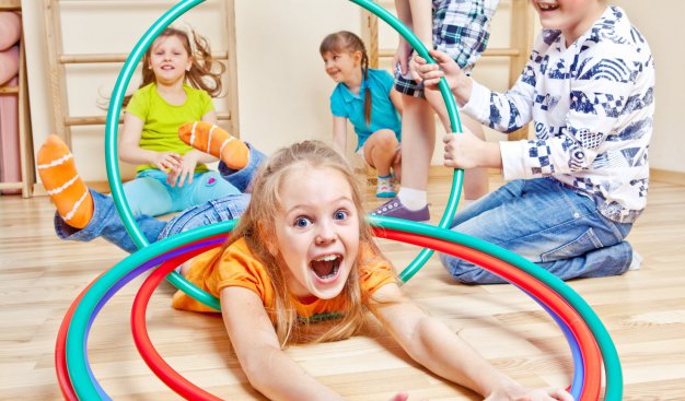 Grupa uśmiechniętych dzieci bawi się na sali gimnastycznej z wykorzystaniem kół hula hop.