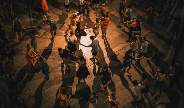 Widok z góry na grupę kilkudziesięciu osób tańczących na drwnianej podłodze, przy lekko przyciemnionym świetle