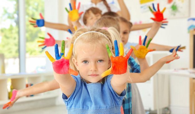 dzieci ustawione jedno za drugim pokazują dłonie pomalowane kolorowymi farbami