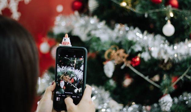 Osoba wykonuje telefonem komórkowym zdjęcie ubranej świątecznej choinki.