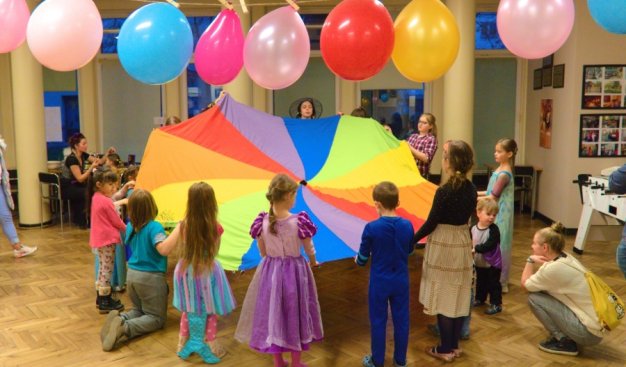 Grupa kolorowo ubranych dzieci, we wnętrzu Wersalika bawiąca siękolorową chustą