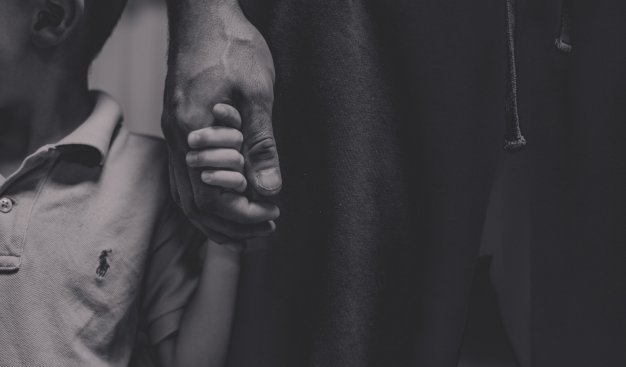 Czarno-białe zdjęcie autorstwa Sebastiana Włodka przedstawiające dłoń dorosłej osoby, ściskającą dłoń dziecka