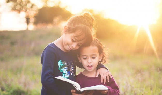 dwójka dzieci na łące w skupieniu czytający książkę
