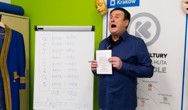 Kierownik Klubu Zakole Jarosław Szwec stojący przy tablicy z ćwiczeniami na dykcję. Szeroko otwiera usta ćwicząc wymowę