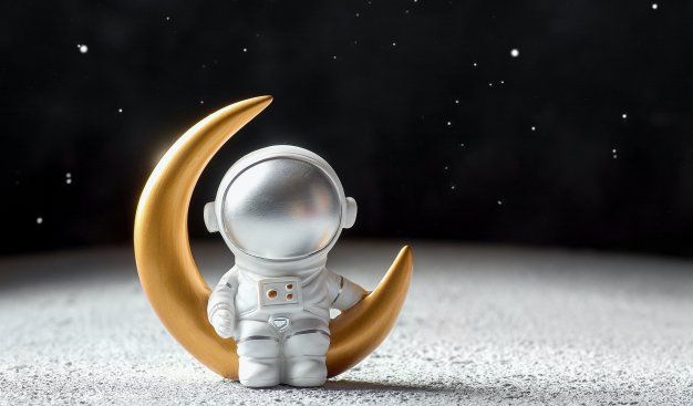 Na biało-czarnym tle imitującym nocne niebo pełne gwiazd umieszczona zostałą figurka kosmonauty siedzącego na pozłacanym księżycu.