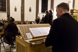Na pierwszym planie znajduję się facet, który gra na starych organach, które znajdują się w kościele. W oddali widzimy resztę zespołu muzycznego.