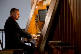 Fotografia przedstawia skupionego, eleganckiego faceta, który bierze udział w koncercie kolęd grając na starym fortepianie.