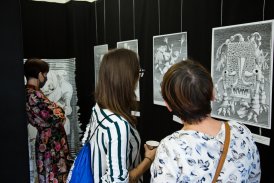 trzy kobiety oglądają wystawę obrazów Daniela Mroza, są odwrócone tyłem, widać tylko ich plecy, za nimi znajdują się cztery obrazy, po lewej stronie większa instalacja, wszystkie obrazy są czarno-białe, przedstawiają fantystyczne postacie