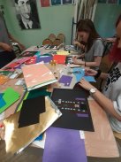 Fotografia przedstawia fragment warsztatów dla młodzieży, gdzie młodzież z różnokolorowych kartek coś wykonuję. Młodzi ludzie są bardzo zaangażowani w warsztaty.