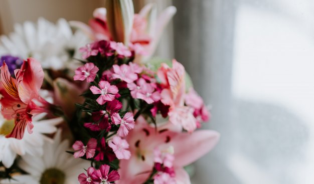 Kolorowy bukiet pełen różnorodnych kwiatów w białych i różowych odcieniach, stojący na parapecie przy oknie.
