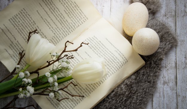 Kompozycja - otwarta książka, bukiet z białymi tulipanami i 2 jajka, leżące na płaszczyźnie z pobielonych desek.
