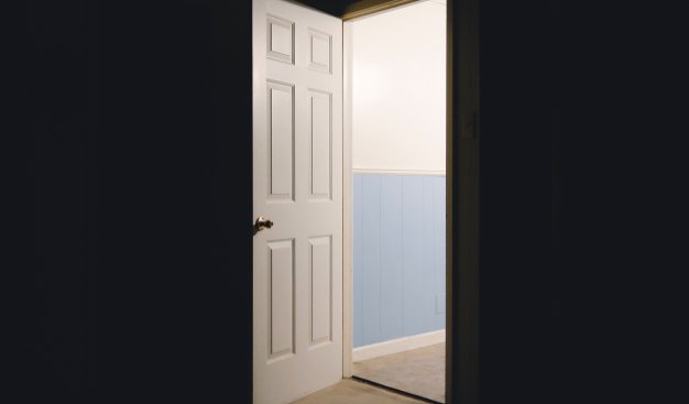 Centralne ujęcie na otwarte drzwi zza których wpada jasne światło.