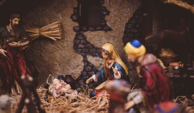 Szopka Bożonarodzeniowa. Pośrodku figurki Maryi i Jezusa na sianie, w tle przy ścianie figurka Józefa. Na pierwszym planie zamazana postać ludzka i figurka wielbłąda.