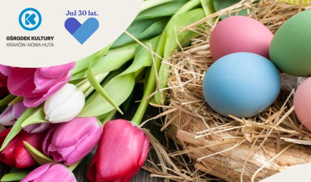 Na drewnianych deskach leży bukiet tulipanów, po prawej słomiana podkładka, a na niej jajka w różnych kolorach.