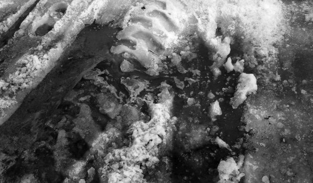 Czarno-białe zdjęcie. Ślad opony w rozstapiającym się śniegu.