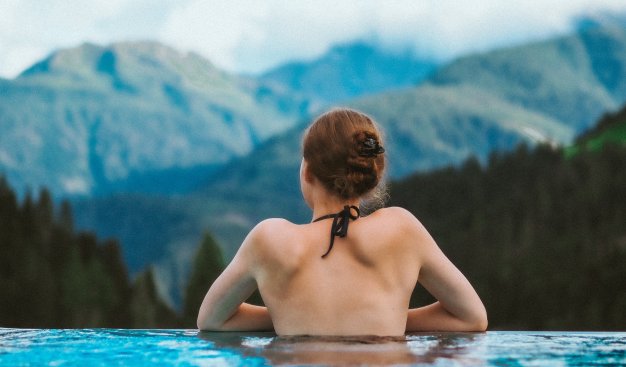 Zdjęcie kobiety stojącej w basenie, tyłem do obiektywu, przodem do widoku gór