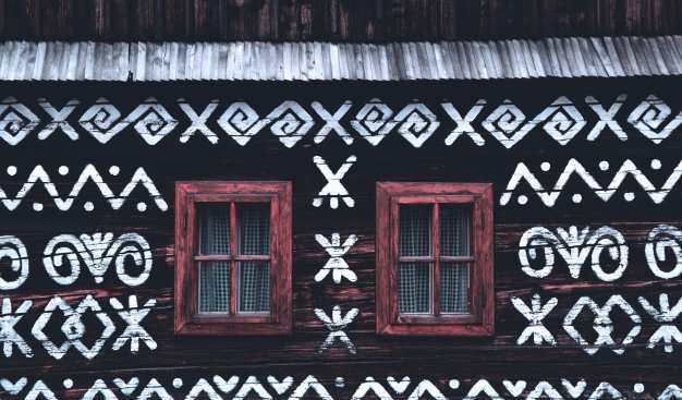 Zdjęcie przedstawiające drewnianą chatę z oknami i folklorystycznym wzorem