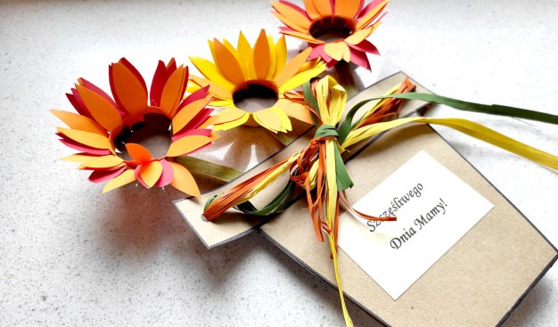 Zdjęcie laurki na Dzień Mamy, z napisem "Szczęśliwego Dnia Mamy". Laurka ozdobiona trzema kolorowymi kwiatami z papieru