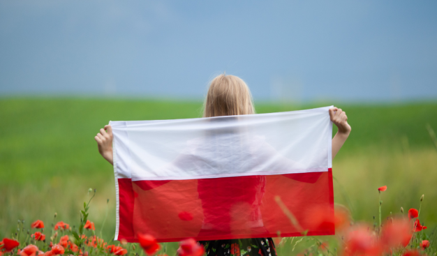 łąka, maki, kobieta stoi tyłem i trzyma flagę Polski