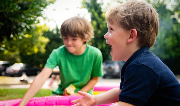 Na zdjęciu dzieci bawiące się na zewnątrz kolorową okrągłą chustą