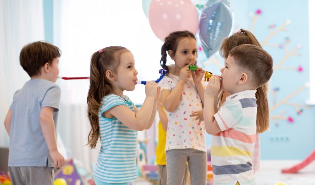 Dzieci w kolorowych strojach. W tle pastelowe balony z helem, confetti. Trwa zabawa.
