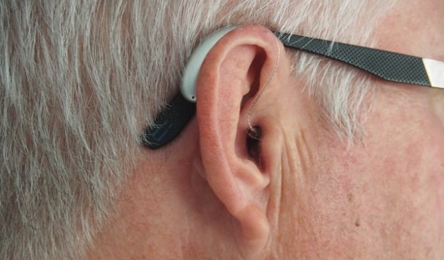 Zdjęcie przedstawiające zbliżenie na męskie ucho, widoczny jest tam także aparat słuchowy
