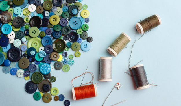 Zdjęcia kolorwych szpulek nici i kolorowych guzików leżących na stole