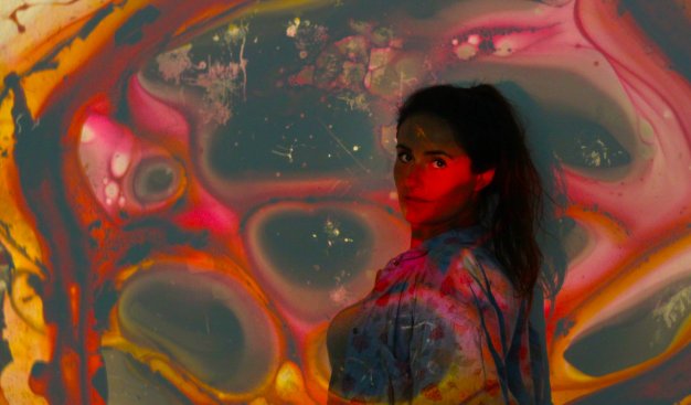 Na zdjęciu Sabina Krauze - instruktorka Klubu Mirage, na tle ściany. Na ścianie i na Sabinie wyświetlany jest kolorowy, abstrakcyjny obraz.