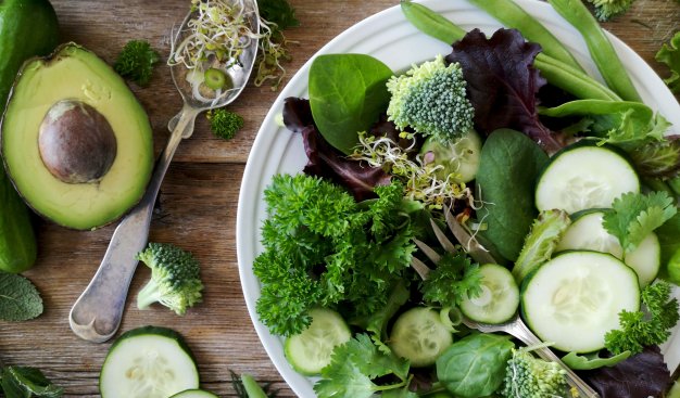 Zdjęcie całej gamy zielonych warzyw - częśc z nich pokrojona jest w formie sałatki na talerzu, reszta leży luźno wokół talerza.
