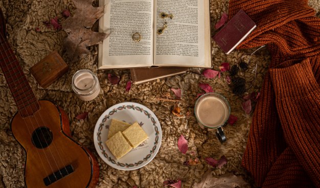 Zdjęcie stołu na którym znajduje się gitara, otwarta ksiązka, filiżanki
