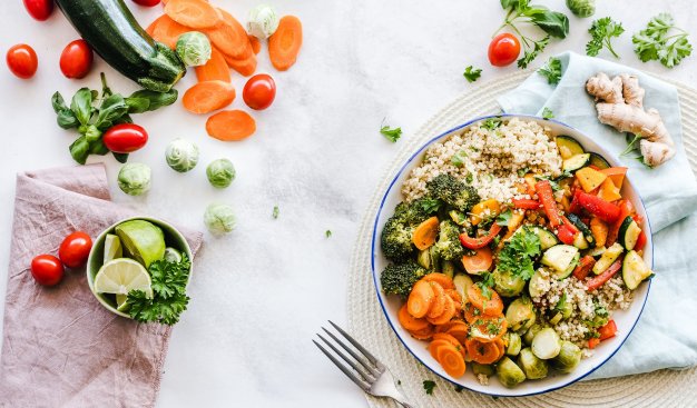 Na stole leży talerz pełen zdrowych i odżywczych warzyw, wokół talerza również leżą luźno rozrzucone pocięte na kawałki kolorowe warzywa.