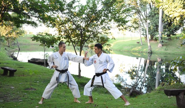 Zdjęcie przedstawiające dwóch mężczyzn trenujących karate, na podwórku, w tle widoczne są drzewa i jezioro