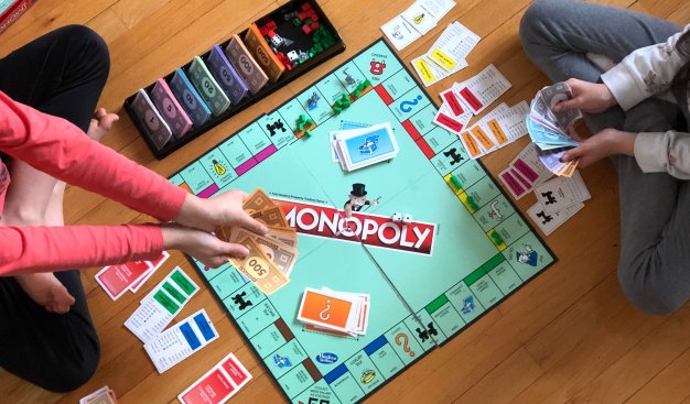 Zdjęcie dzieci grających na ziemi w grę planszową Monopoly.