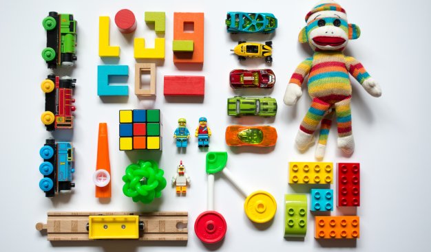 Na białej planszy widzimy z góry regularnie ułożone zabawki - klocki, drewniany pociąg z wagoanmi, maskotkę, samochodziki, inne drewniane zabawki o geometrycznych kształtach.