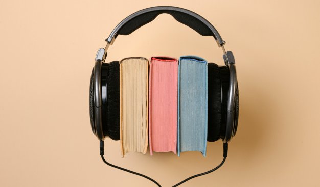 Trzy kolorowe książki widziane od góry, na które założone są czarne duże słuchawki.