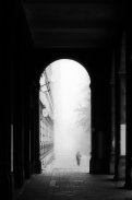 Czarno-białe zdjęcie bramy i postaci po prawej stronie idącej we mgle