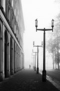 Czarno białe zdjęcie ulicy we mgle, w tle znajduje się postać.