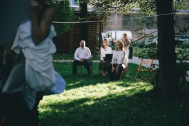 Scena z plenerowego spektaklu, na której są cztery młode osoby, siedzące w ogrodzie. W bliskiej odległości od siebie. Trzymają oni w swoich rękach instrumenty.