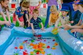 Na zdjęciu dzieci napełniające pompowany basen, kolorowymi galaretkami.