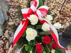 Wieniec ozdobny z biało-czerwonymi kwiatami i wstęgą złożony przy pomniku upamiętniającym ofiary zbrodni katyńskiej.