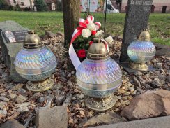 Trzy szklane znicze oraz wieniec ozdobny z biało-czerwonymi kwiatami i wstęgą złożone przy pomniku upamiętniającym ofiary zbrodni katyńskiej.