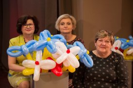 Fotografia przedstawiająca trzy siedzące obok siebie kobiety, w Klubie Dukat. Przed dwoma paniami stoi pudełko z balonami, w kształcie kwiatów. Balony są w kolorach flagi Polski oraz Ukrainy.