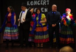 Fotografia przedstawiająca cztery kobiety oraz dwóch mężczyzn, stojących na scenie, w Klubie Dukat. Kobiety ubrane są w kolorowe bluzki i spódnice, a mężczyźni w garnitury.  Dziewczyny na szyi mają szal boa z piór.
W tle biały napis " Koncert Życzeń", przypięty na czarnym tle.