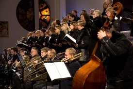 Fotografia przedstawia grupę ludzi, którzy biorą udział w koncercie kolęd, grając na różnych instrumentach oraz śpiewając w chórze.