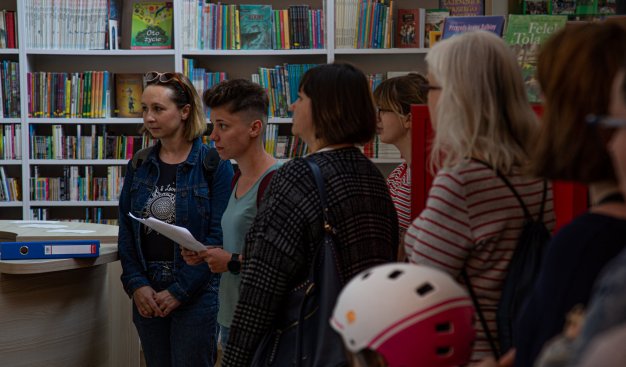 Zdjęcie przedstawia grupkę osób stojąca na tle regałów bibliotecznych z książkami