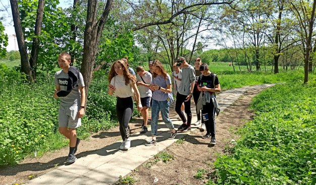 Zdjęcie przedstawiające grupkę nastolatków idących przez tereny zielone, ze smartfonami w rękach