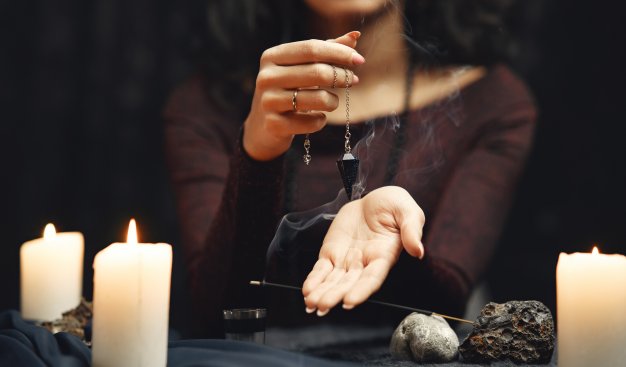 Zdjęcie kobiety trzymającej w dłoni naszyjnik, na pierwszym planie znajdują się zapalone świeczki