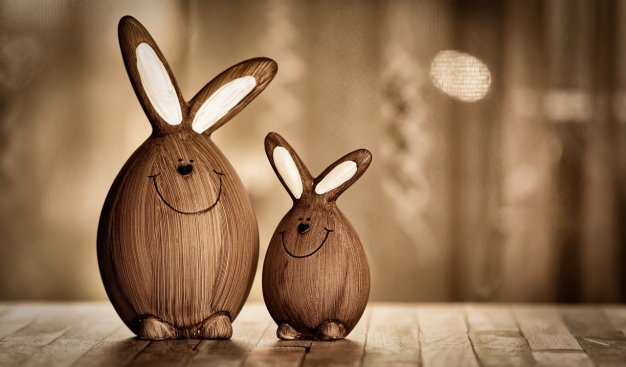 Dwa drewniane zające - mniejszy i większy - w kształcie jajek z doklejownymi długimi uszami, z narysowanym uśmiechem.